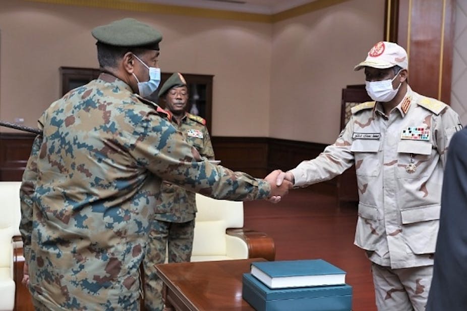 Two men in military uniforms and medical face masks shake hands.
