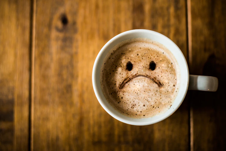A cup of coffee with a sad face emoji.