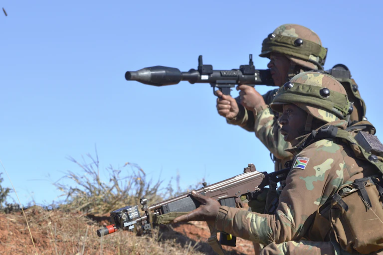 Two men in camouflage uniform, pointing weapons