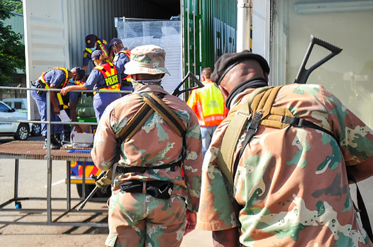 Two soldiers watch as police search a truck.
