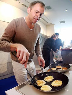 Man uses a spatula to flip pancakes in a frying pan.