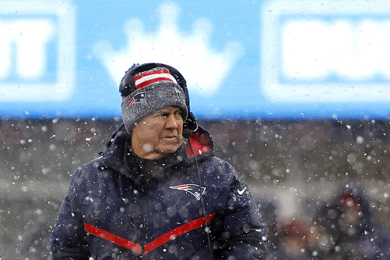 Older man wearing a headset, a knit cap and a winter coat glances to his left surrounded by snow flurries.