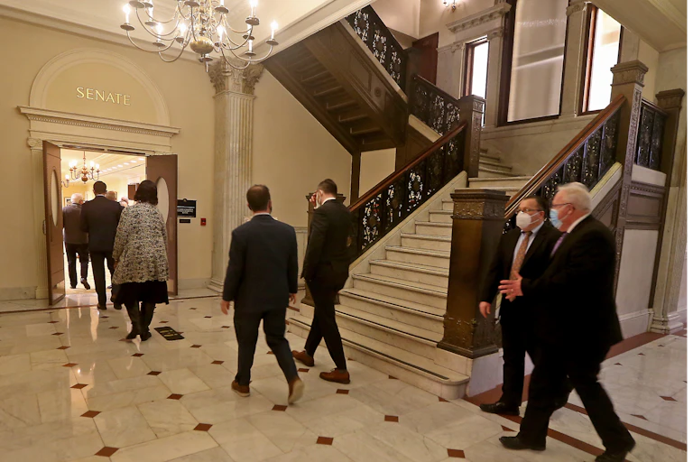 people wearing suits walk under chandelier through door marked 'SENATE'