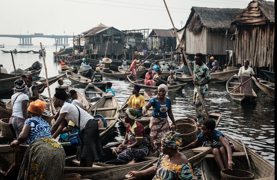 Women in canoes gather in groups close to houses on stilts.