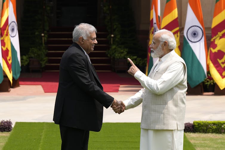 A man in a white Nehru jacket gestures while talking to a man in a suit.