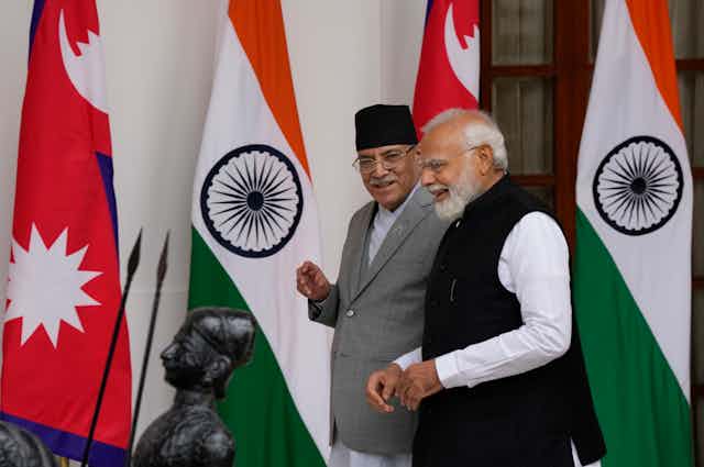 Two men, one in a black fez, smile as they walk beside eachother with red white and green flags behind them.
