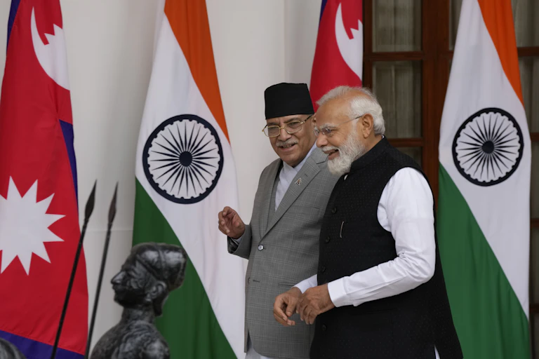 Two men, one in a black fez, smile as they walk beside eachother with red white and green flags behind them.
