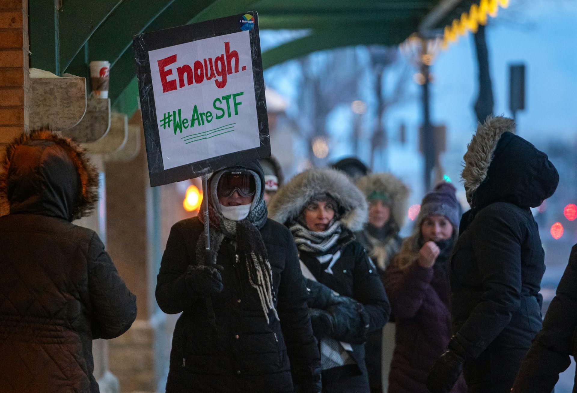 People seen with signs dressed in winter coats outdoors.