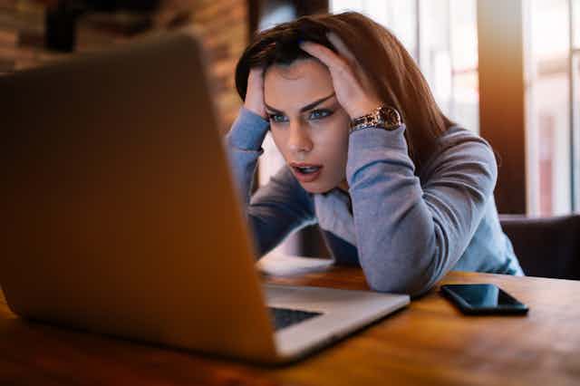 A young woman looks in disbelief at her laptop computer