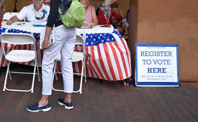 A voter registration table with red-white-and-blue design but no partisan markings.