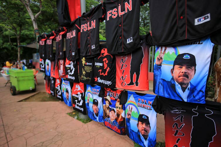 T-shirts with pictures of a man in a blue jacket making a 'V' sign with his fingers, and shirts that say 'FSLN,' hang on display outside.
