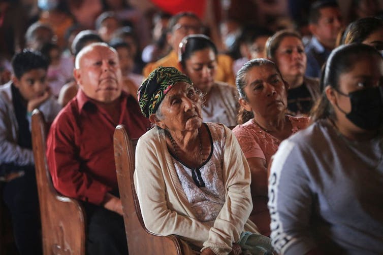 Several rows of people seated in church pews, all looking ahead.