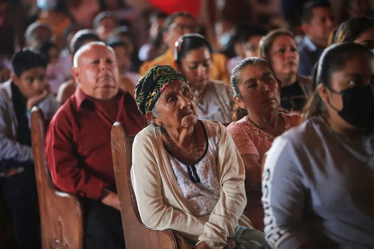 Several rows of people seated in church pews, all looking ahead.