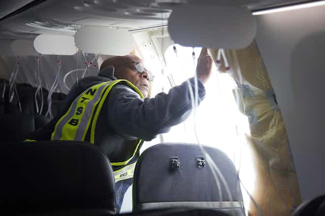 A person wearing a reflective vest looks at an opening in the side of a passenger aircraft.