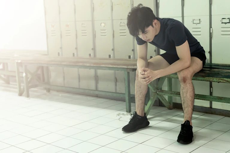 A young man sitting alone on a bench in a locker room