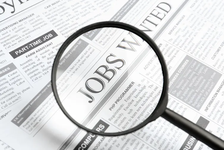 A magnifying glass hovering over a newspaper page that says 'Jobs Wanted.'