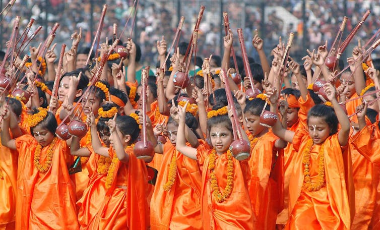 Girls in orange flowing dresses dance.