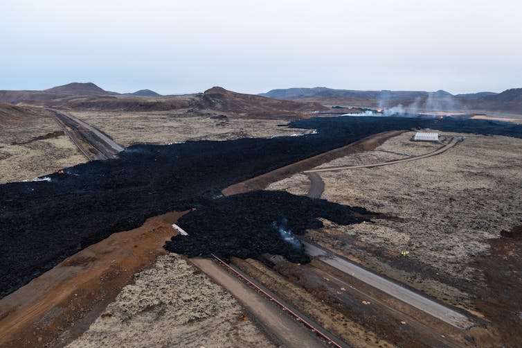 An earthen berm with black lava along the one side of it. The lava broke through along a highway.