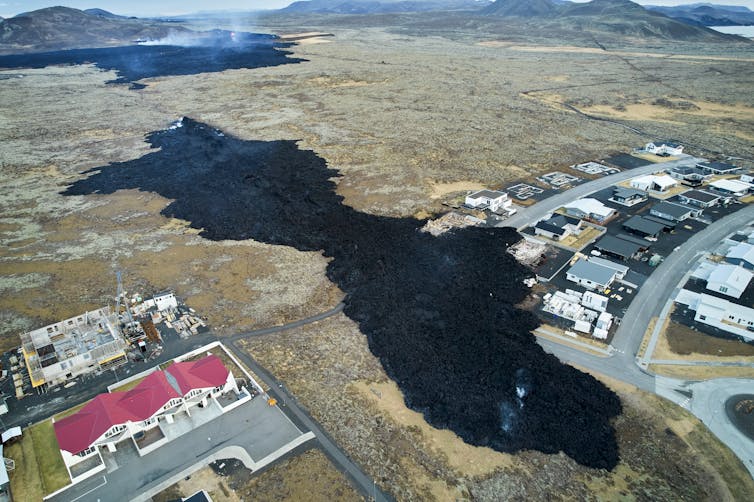Black lava engulfs the edge of a neighborhood, leaving homes in ruins.