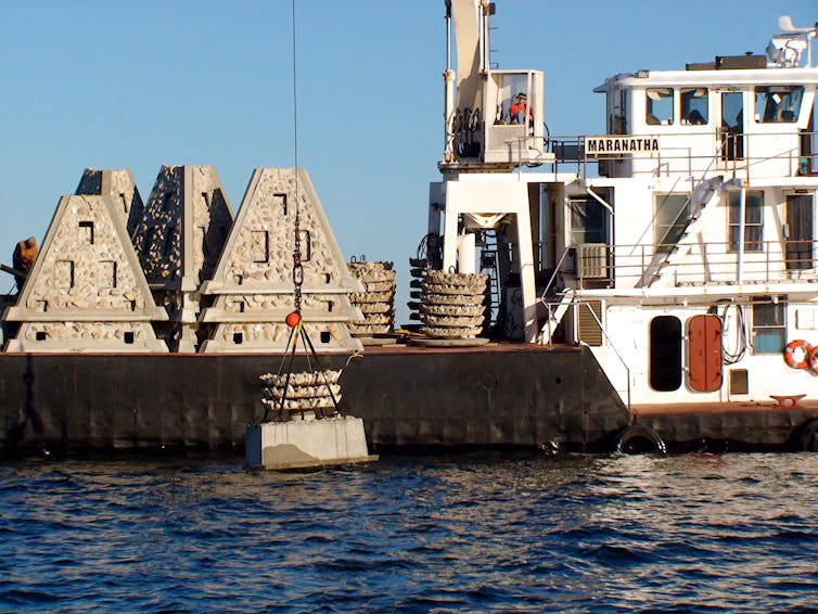 A boat with a crane lowers pyramid-shaped structures into the water.