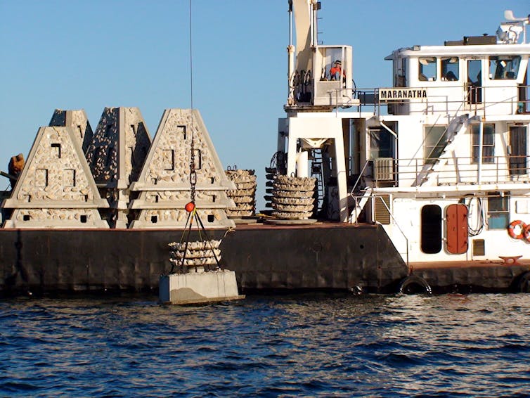 A boat with a crane lowers pyramid-shaped structures into the water.