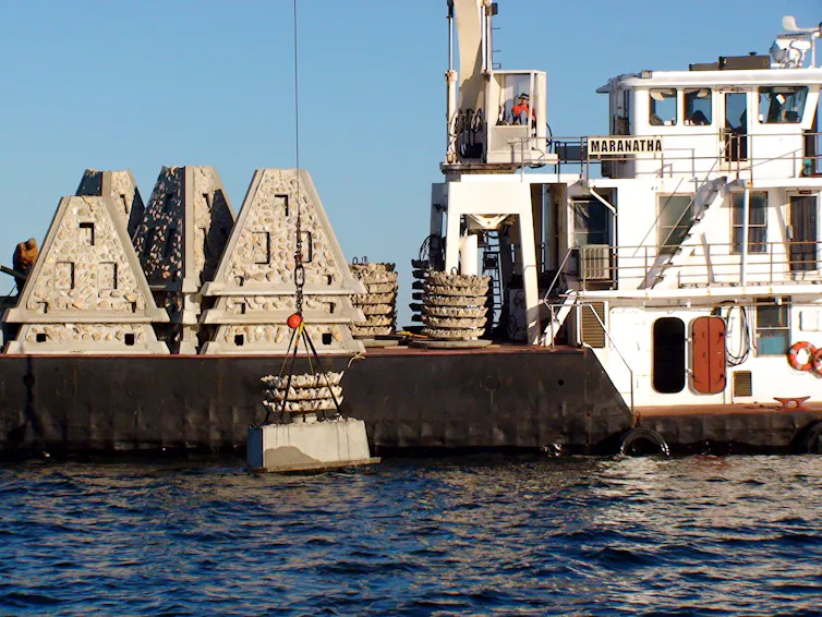 A boat with a crane lowers pyramid-shaped structures into the water.