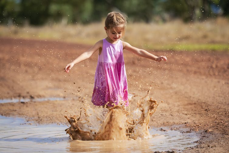 girl in pink dress plays in muddy puddle