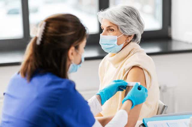 A health-care workers applies a bandaid to the upper arm of a senior woman.