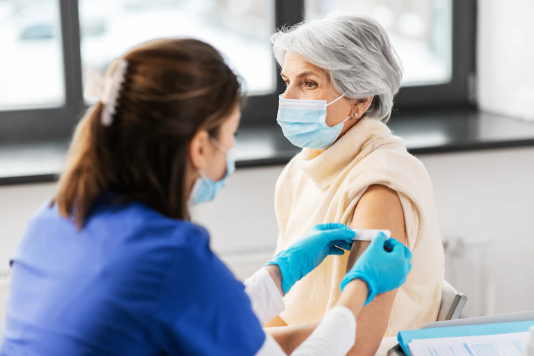 A health-care workers applies a bandaid to the upper arm of a senior woman.