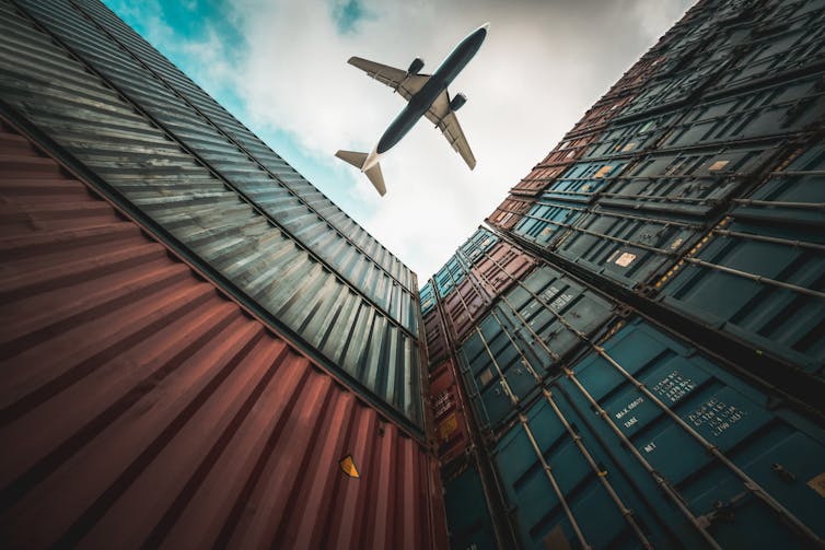 A freight airplane flying above shipping containers.