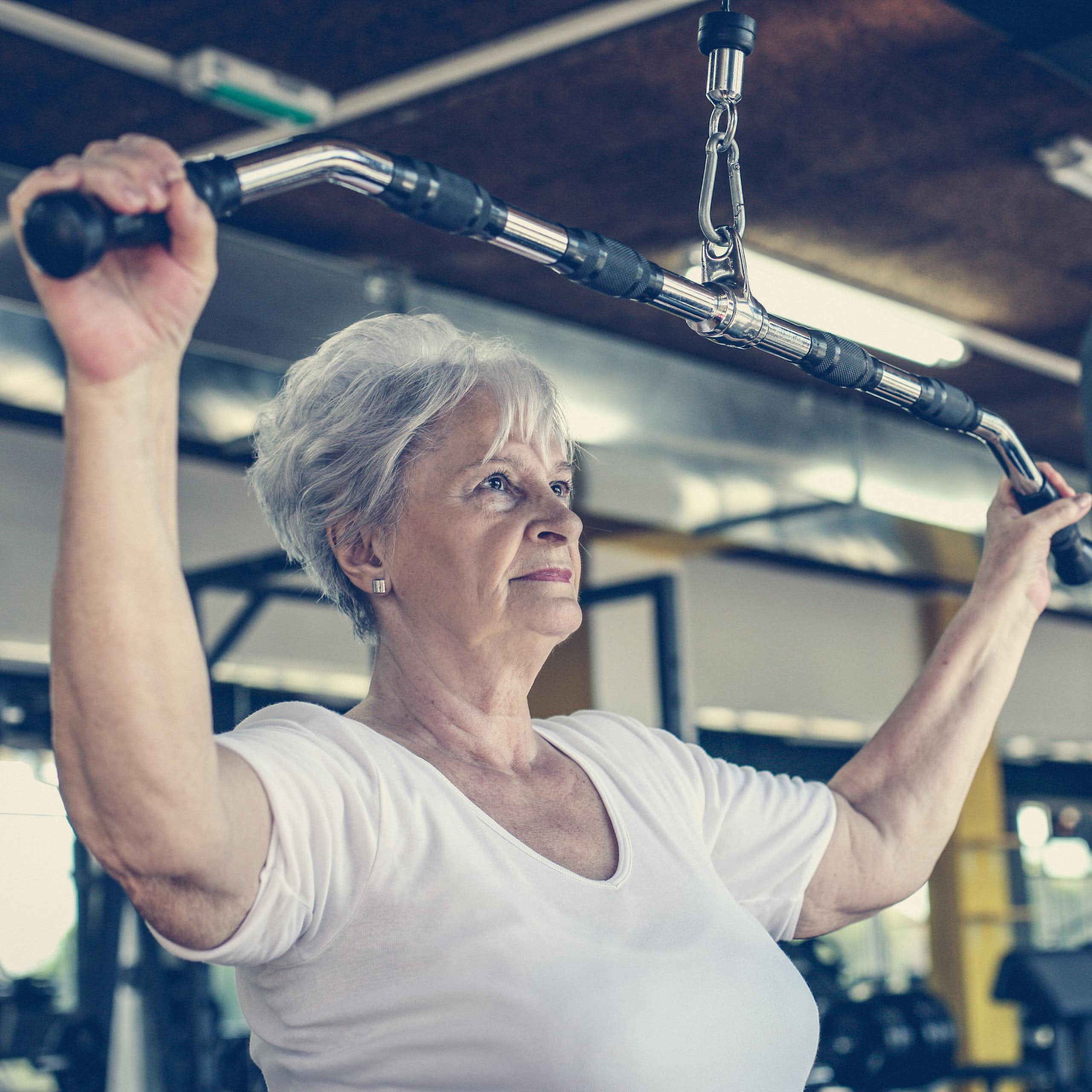 An older woman uses an exercise machine to train her arm muscles.