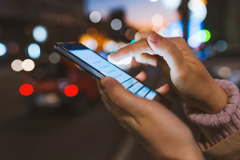 Close up of a woman's hands scrolling on a smartphone outdoors in a city at night