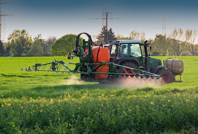 A tractor equipped with a tank spraying chemicals on a crop.