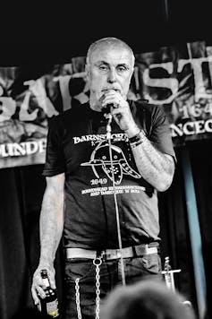 Punk poet Attila holds a microphone in one hand and beer in the other.