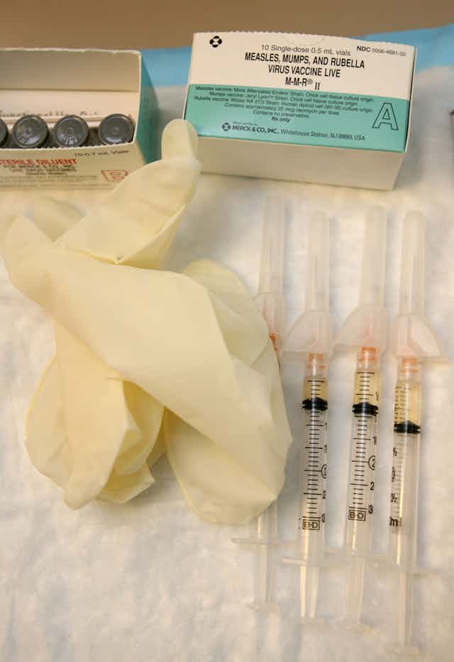 An open box of MMR vaccine, an open box, containing four vials of the vaccine, a pair of disposable medical gloves and four syringes containing the vaccine