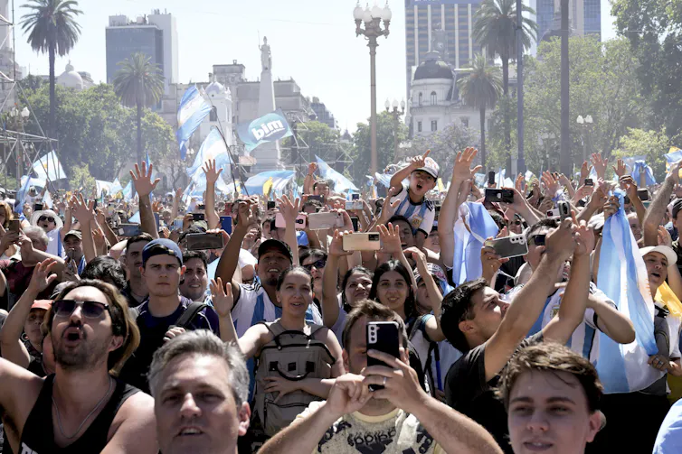 People march down a street, carrying Argentine flags