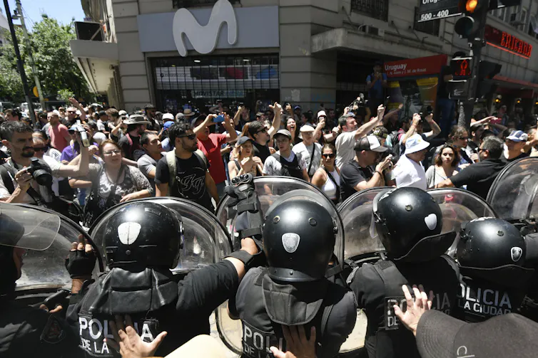 People demonstrate with fists raised in front of a row of police officers