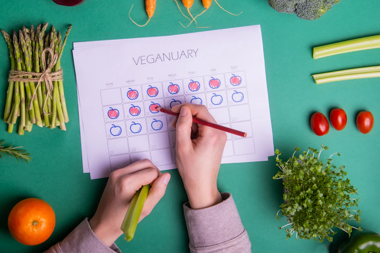 A hand drawing apples on days in a calendar marked 'Veganuary' surrounded by vegetables.