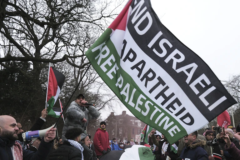 A crowd waves red, white, green and black flags, with one reading End Israeli Apartheid, Free Palestine.
