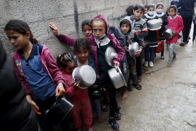 A line of children hold pots as they wait.