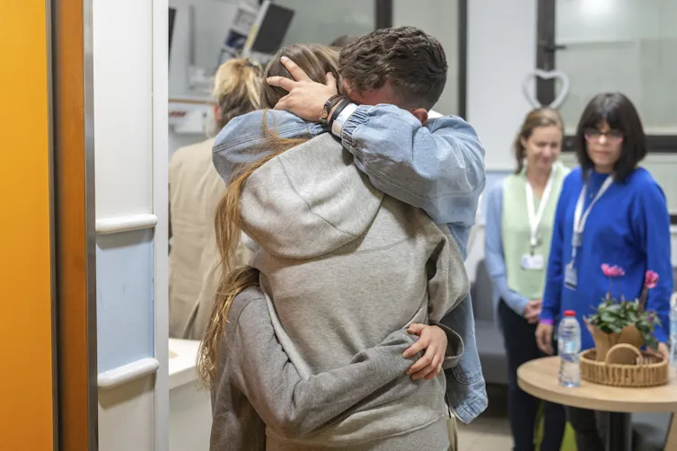 A woman with long blond hair is tightly embraced by her family members.