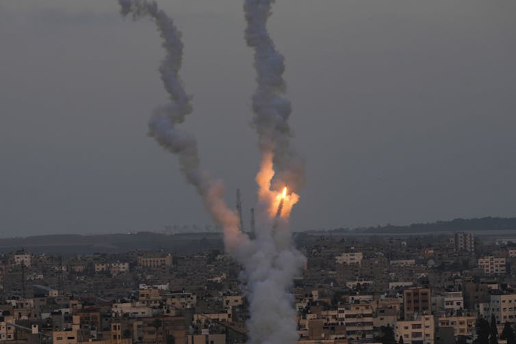 Plumes of fiery smoke from rockets fly over an urban area.