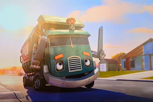 A still from the animated series Trash Truck showing a boy riding on top of the truck down a suburban street