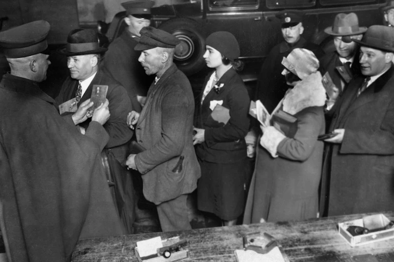 1930 black and white photo of people lined up and officer looking at a passport