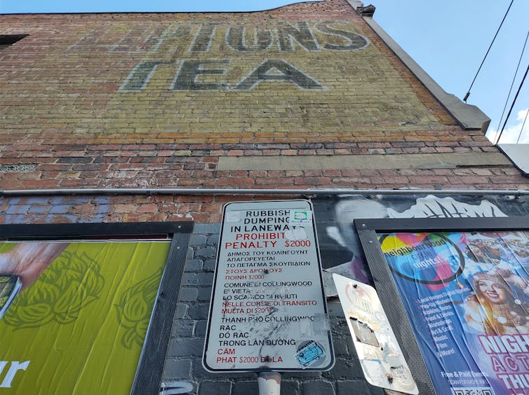 A commercial Lipton Tea sign painted on a wall above 2 official signs about restrictions, with stickers put over them, flanked by large advertising posters