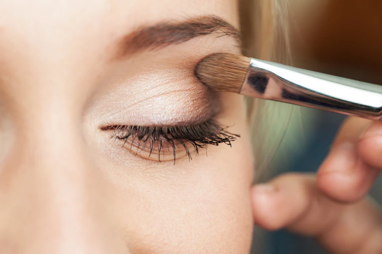 Gros plan sur l'oeil d'une femme qui est en train d'appliquer un fard à paupières.