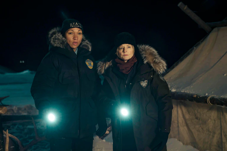Jodie Foster and Kali Reis dressed as detectives, shining torches in the dark.