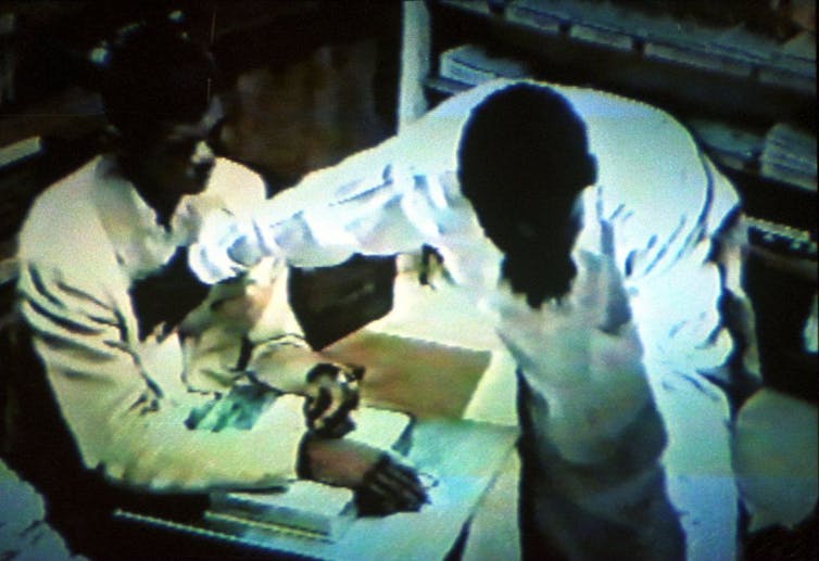A grainy image of a man wearing white holding a hand to the chest of a seated man.