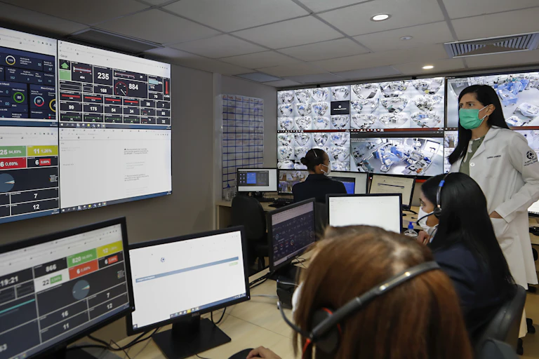 Médica e assistentes trabalham numa sala cheia de computadores e painéis digitais