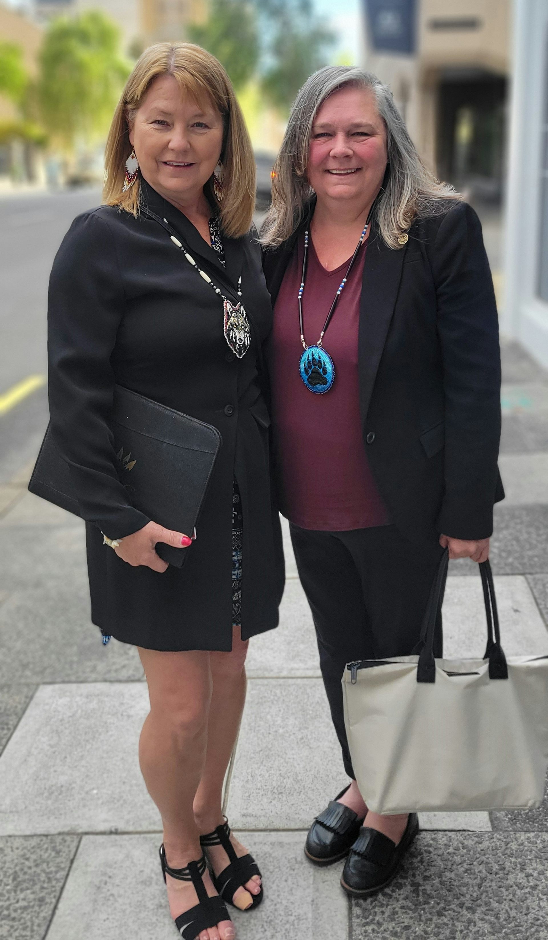 Two women pose for a photo on a sidewalk.